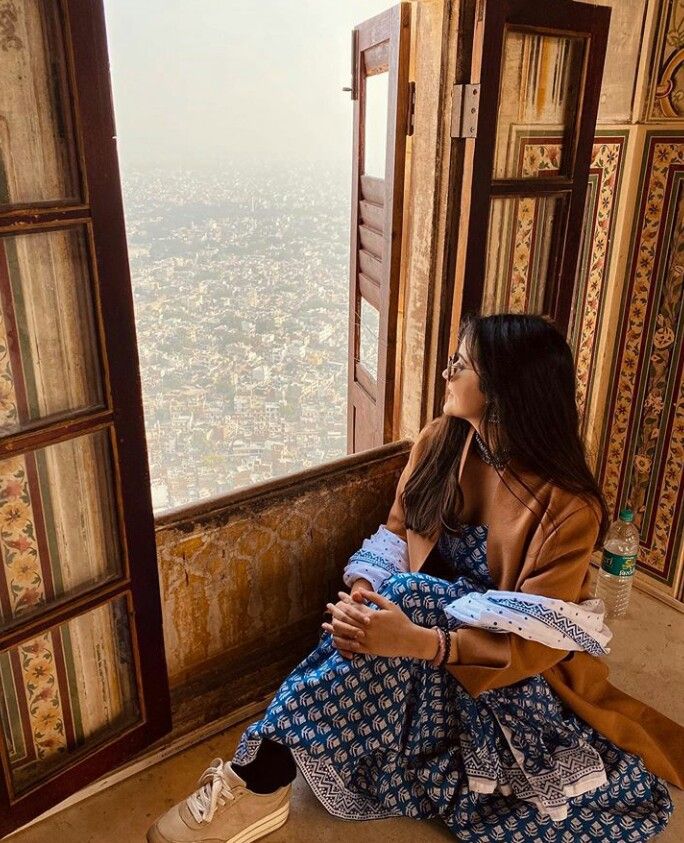 a woman sitting on top of a window sill looking out at the city below