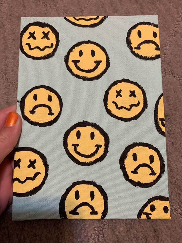 a hand holding up a piece of paper with yellow and black smiley faces on it