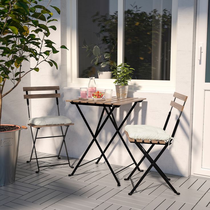 two chairs and a table on a porch next to a potted plant in front of a window