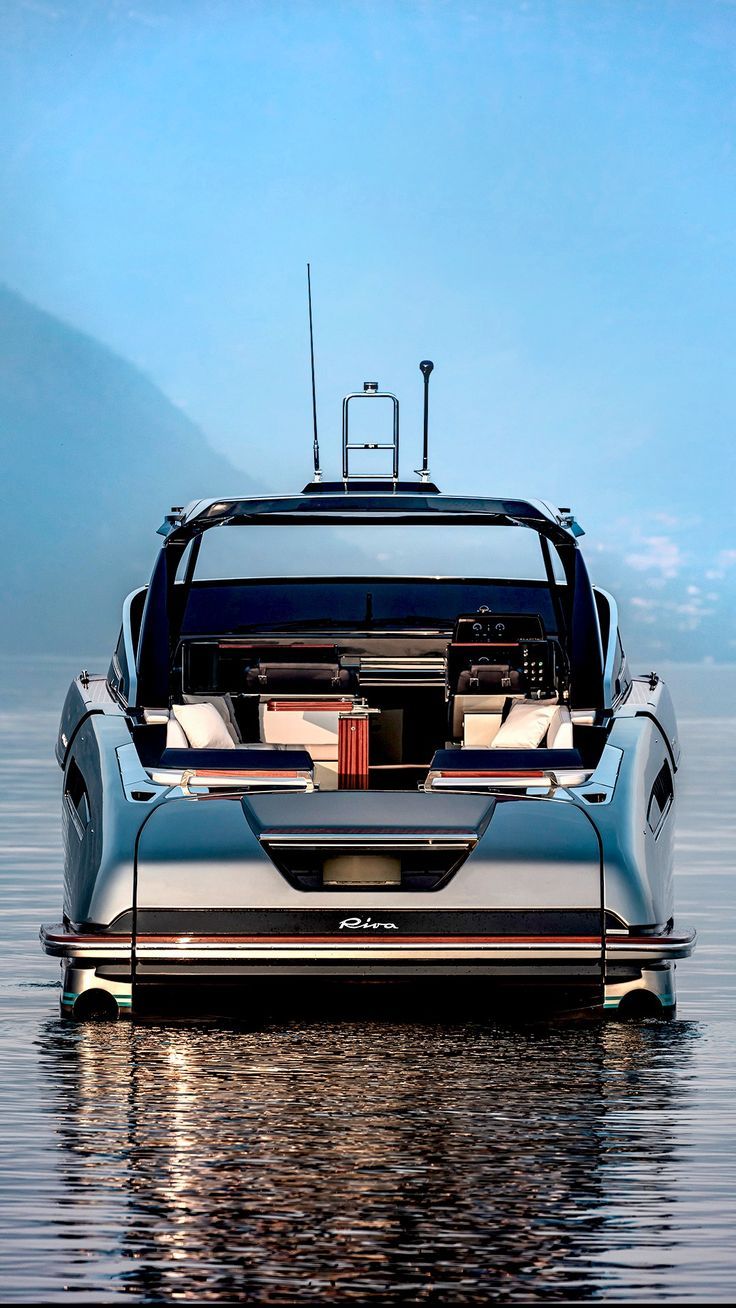 the back end of a car with its hood open on water in front of mountains