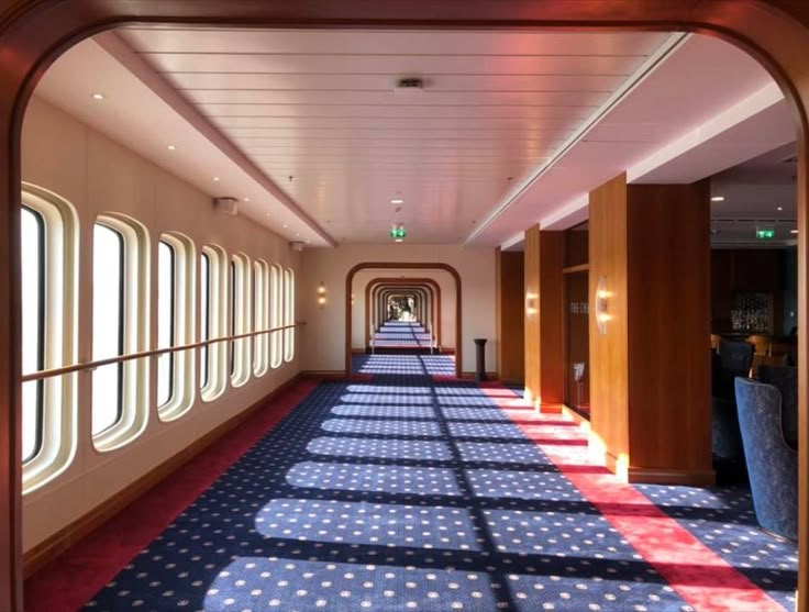 a long hallway with blue and red carpeted flooring next to large windows on both sides