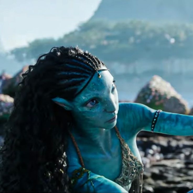 a woman with blue makeup and long hair pointing at something in the distance while standing on rocks