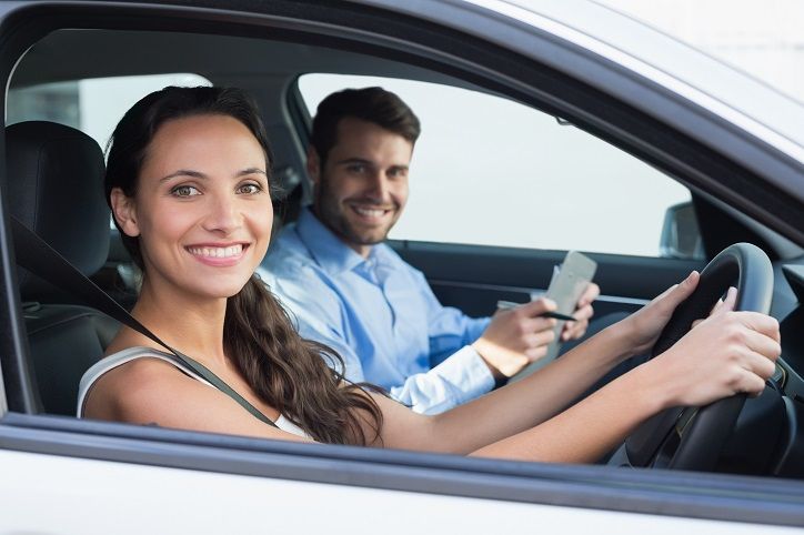 a man and woman sitting in the driver's seat of a car, both smiling at the camera