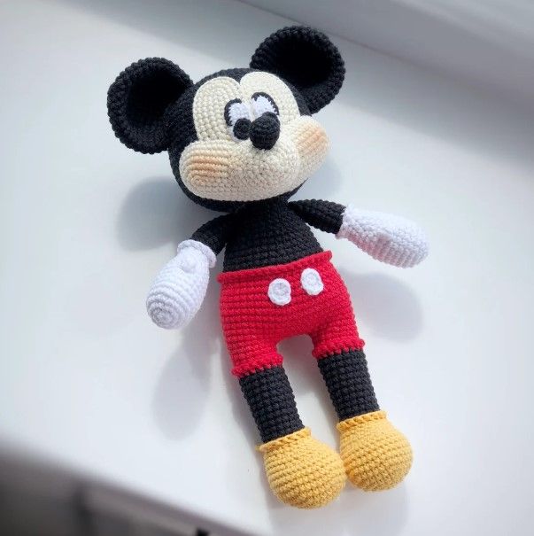 a crocheted mickey mouse doll laying on top of a white table with the words,