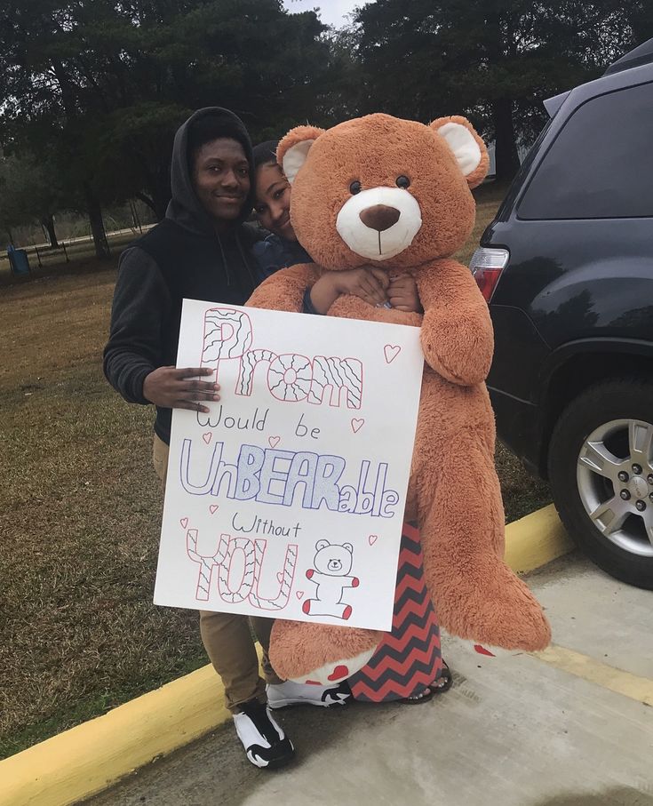 a person holding a large teddy bear in front of a car with a sign on it