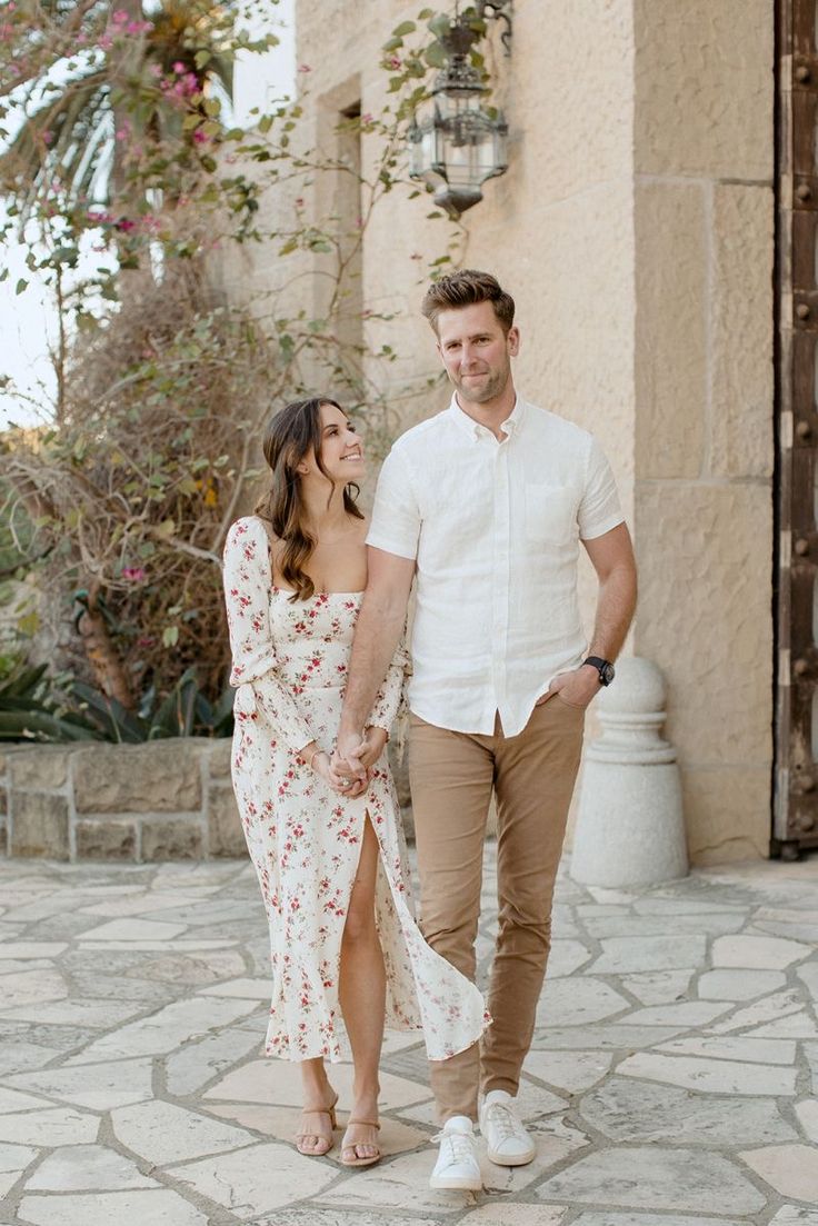 a man and woman are holding hands while walking down the stone walkway in front of a building