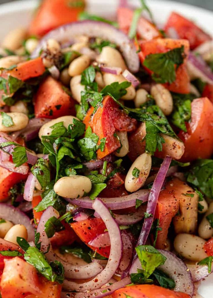 a white plate topped with lots of veggies next to red onion and beans