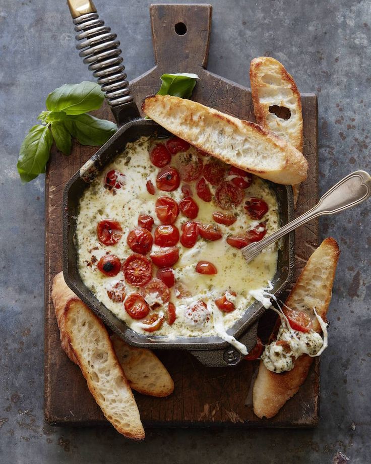 a pan filled with bread and tomatoes on top of a cutting board next to some slices of bread