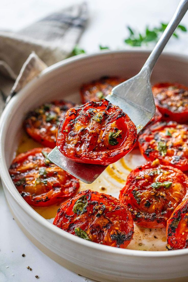 a white bowl filled with sliced tomatoes on top of a table next to a fork