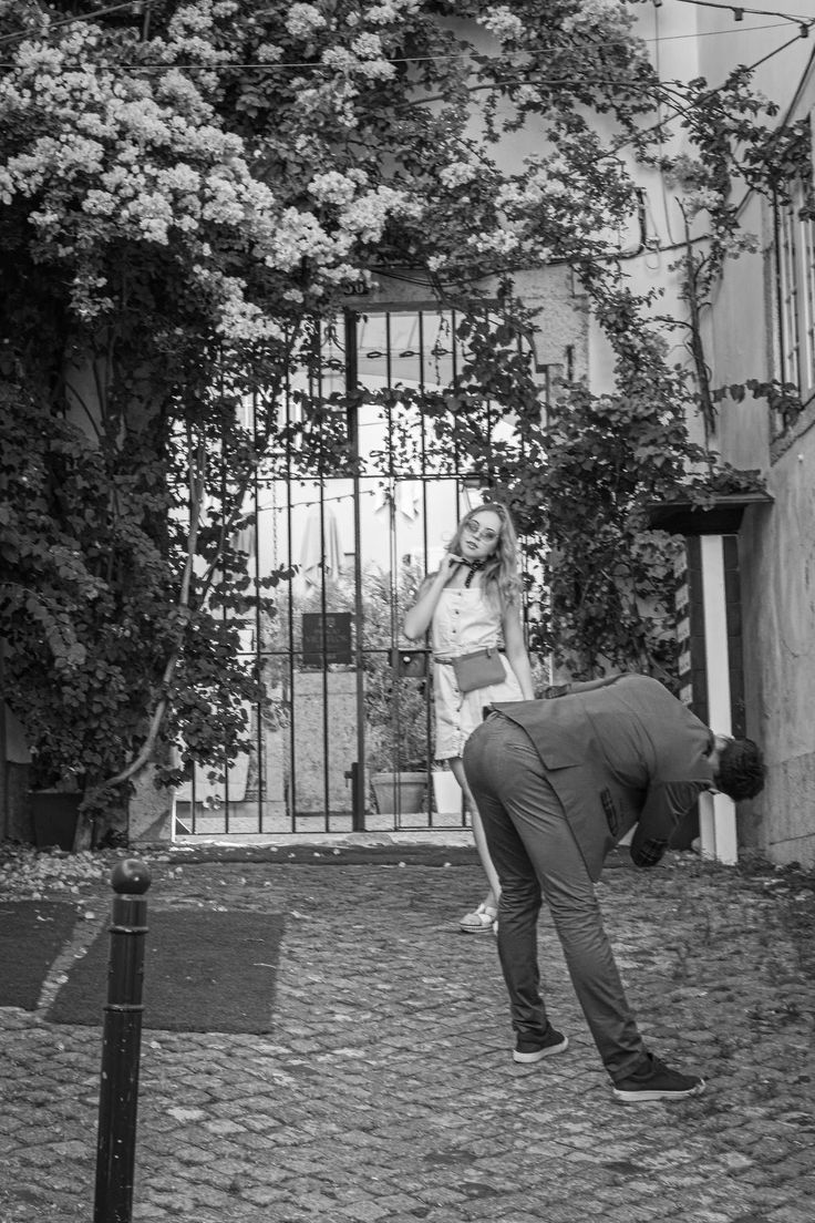 a man and woman standing in front of a gate with flowers growing on the wall