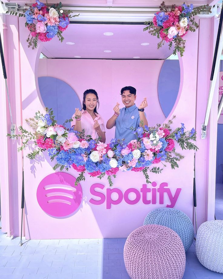 two people standing in front of a spotify sign with flowers on the wall behind them