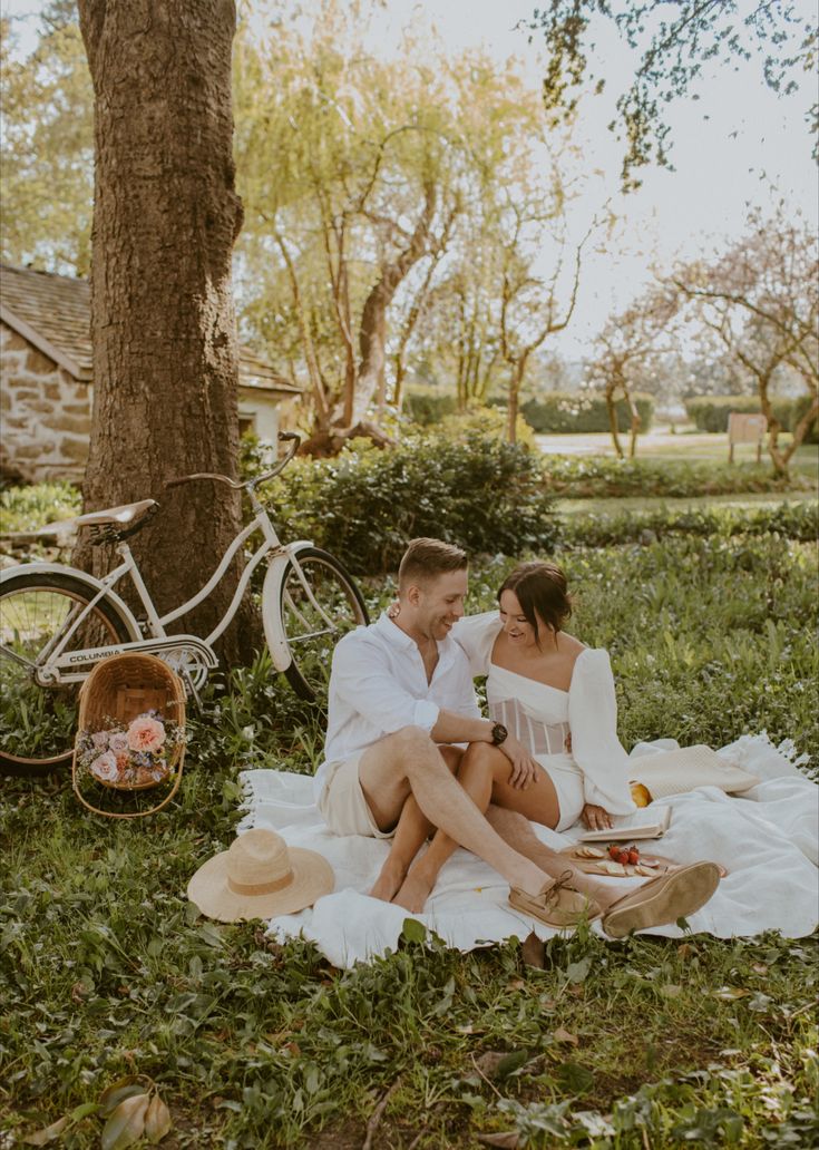 a man and woman sitting on the grass under a tree