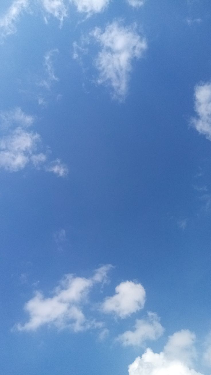 an airplane is flying high in the blue sky with white clouds and green grass below