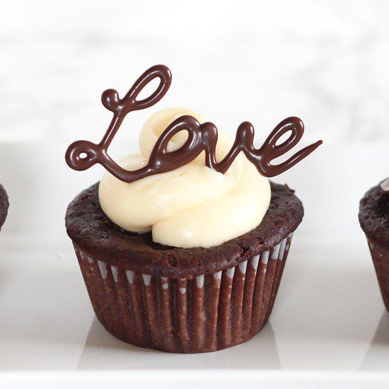 three chocolate cupcakes with white frosting and the word love spelled on top