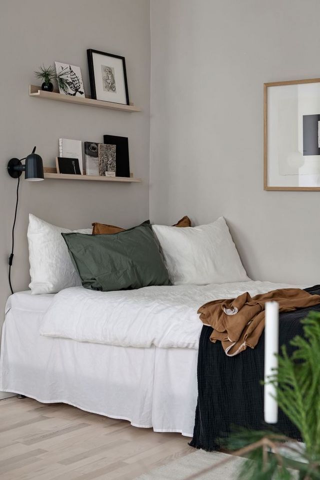 a white bed sitting in a bedroom next to a wooden shelf filled with pictures and plants