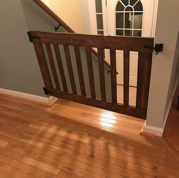 an open wooden gate in front of a door on a hardwood floor with stairs leading up to it