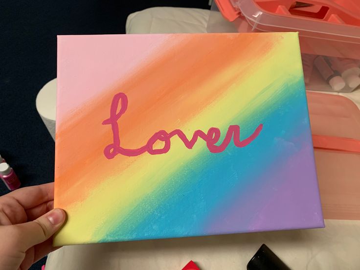 someone is holding up a painted canvas with the word love on it and some crayons