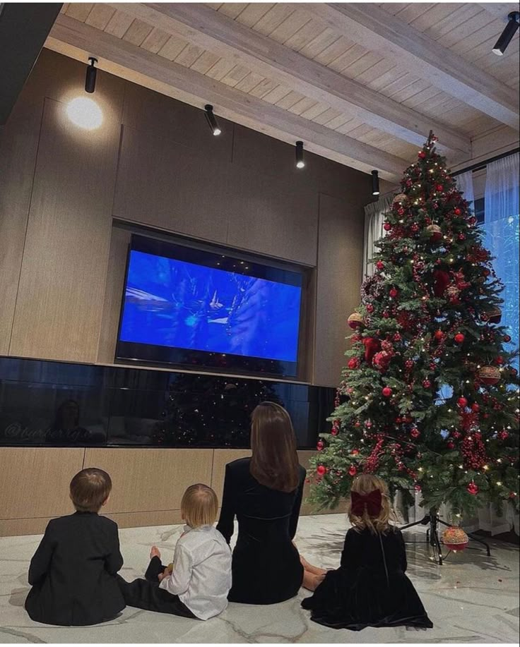 three children sitting in front of a christmas tree watching tv