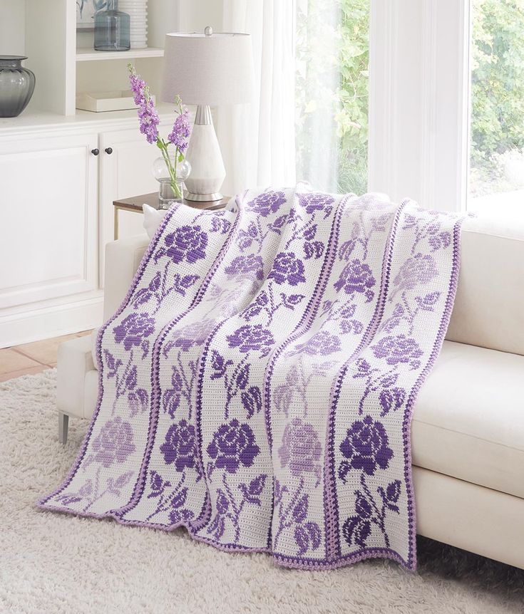 a living room with a white couch and purple flowered blanket on top of it