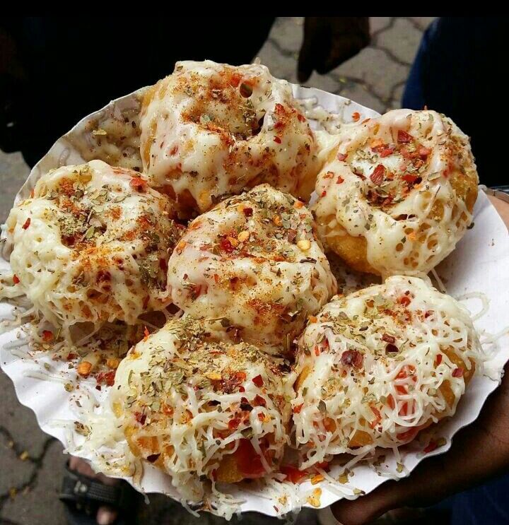 a person holding a plate full of doughnuts covered in cheese and toppings