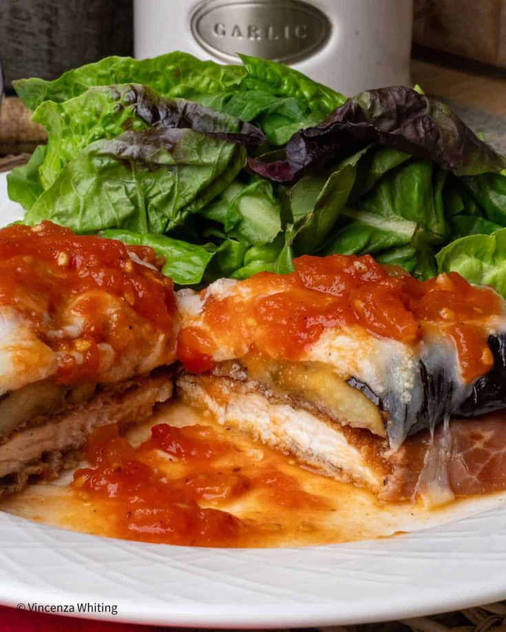 a white plate topped with lasagna covered in sauce next to a green salad