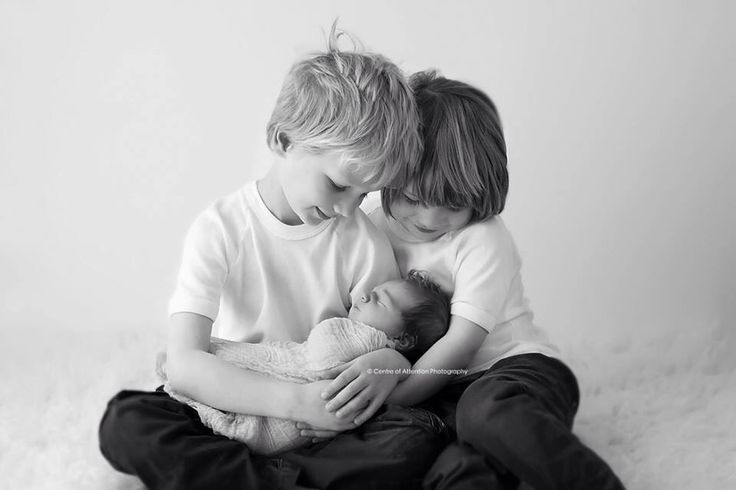 two young boys cuddle together while holding a baby