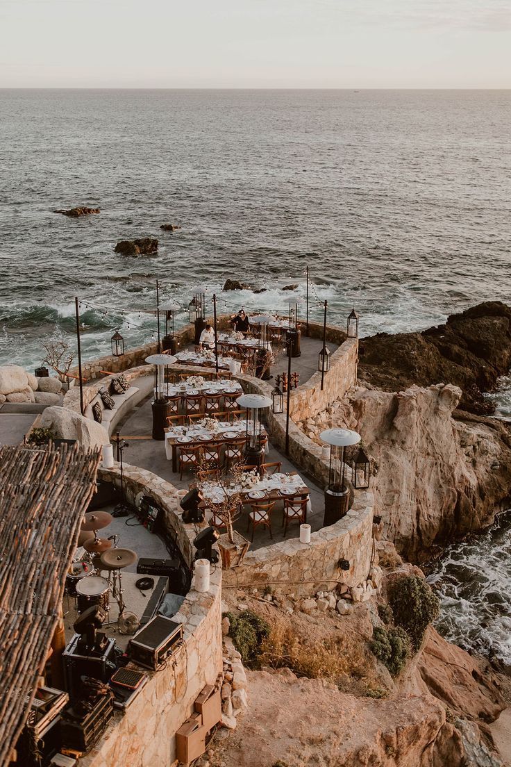 an outdoor dining area next to the ocean with tables and chairs set up on it