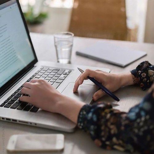 a woman sitting at a table with a laptop and pen in front of her computer