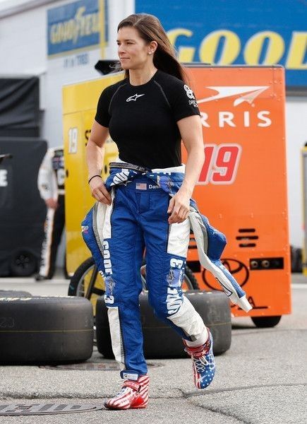 a woman in black shirt and blue pants walking on street next to tire tracks with tires behind her