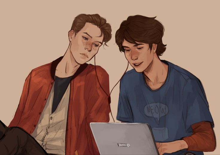 two young men sitting next to each other looking at a laptop