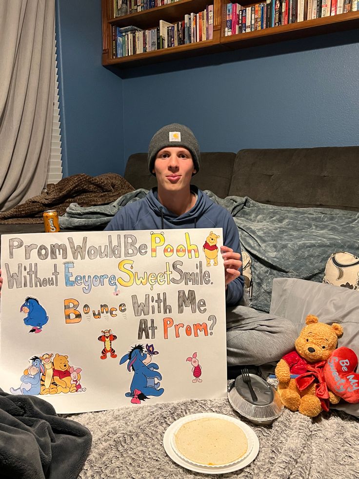 a young man holding up a sign with winnie the pooh written on it in front of him