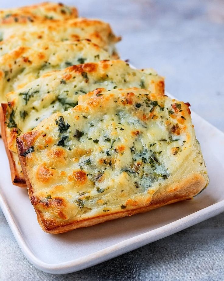 three pieces of bread with cheese and spinach on it sitting on a white plate