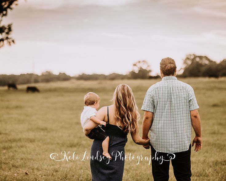 a man and woman holding a baby in their arms while walking through an open field