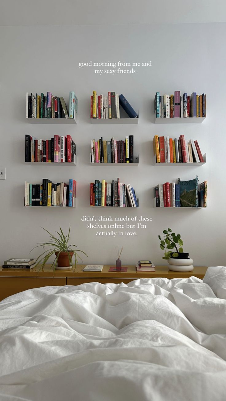 there is a bed with white sheets and books on the shelves above it that are filled with books