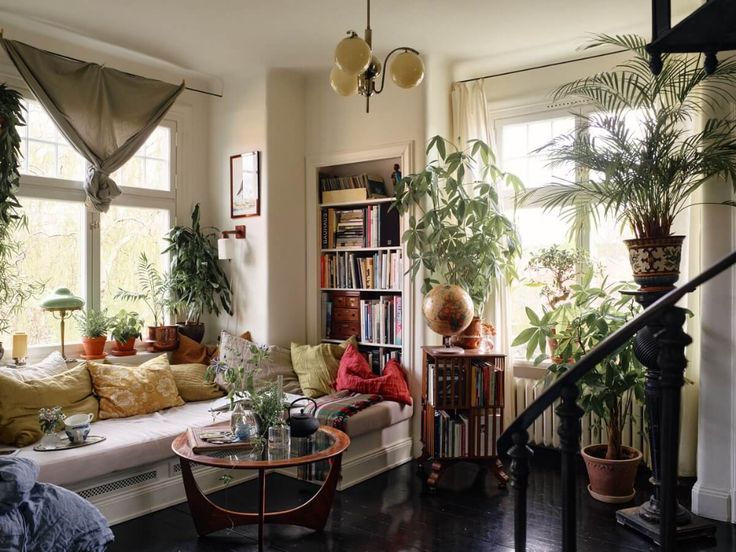 a living room filled with furniture and lots of plants on the windows sill next to a bookshelf