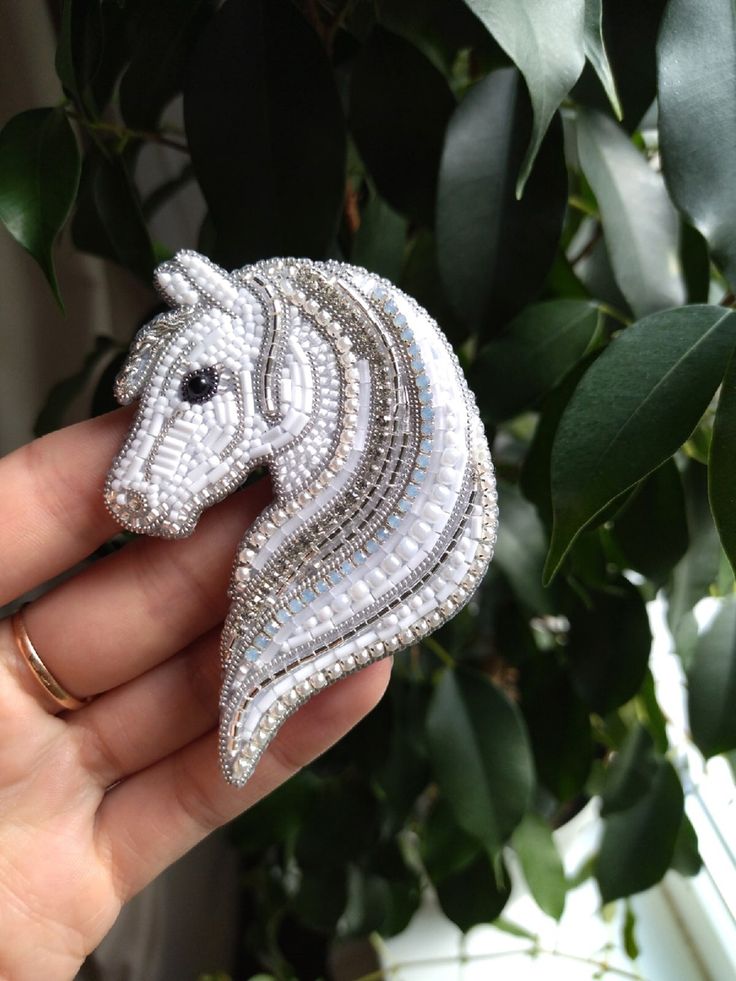 a person holding a brooch with a horse on it's back in front of a plant