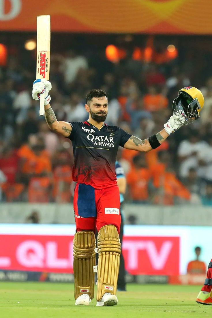 a cricket player holding his bat and helmet in the air while standing on a field