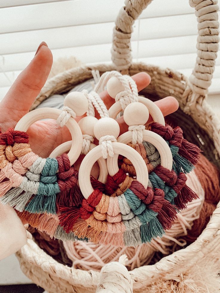 a hand holding several pieces of yarn in a woven basket with rope handles and tassels