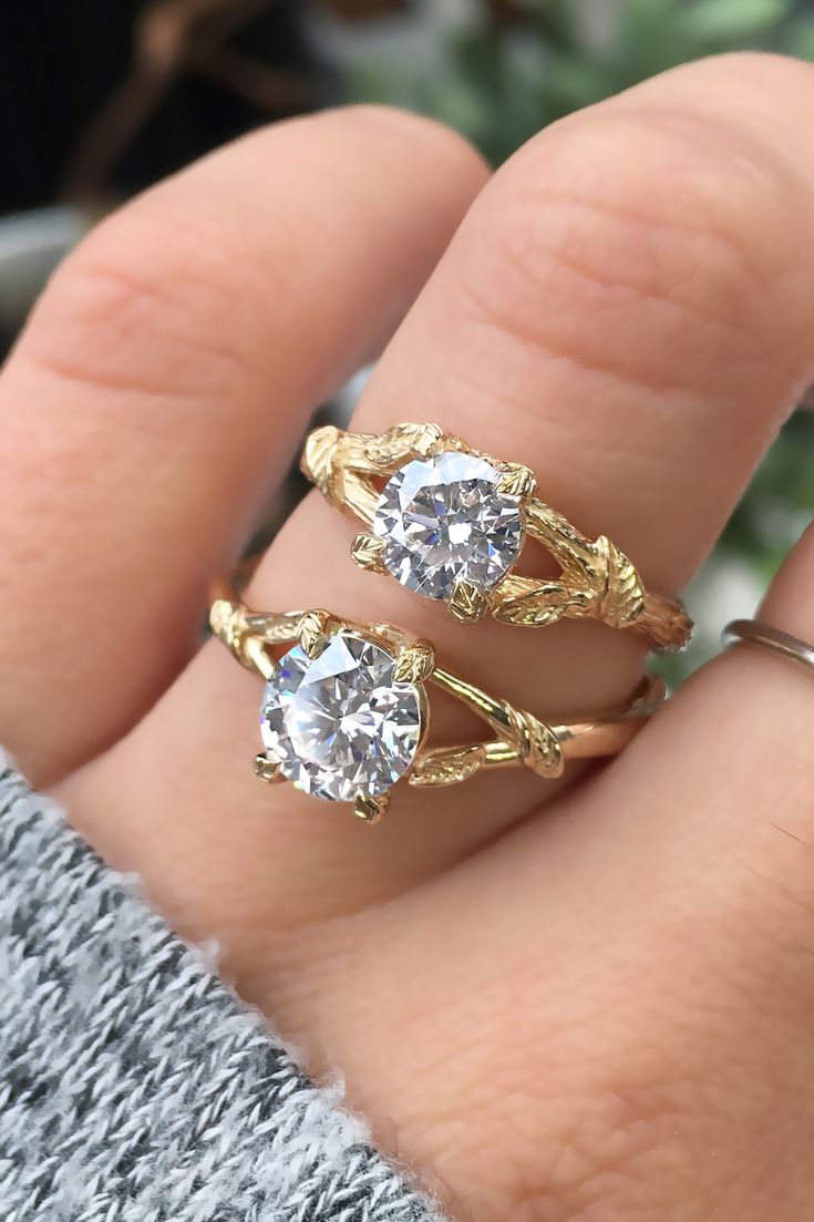 two gold rings with white diamonds on each one and the other hand holding it up