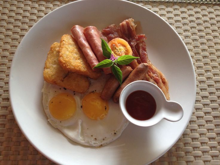 a white plate topped with eggs, sausages and other breakfast foods next to a cup of coffee