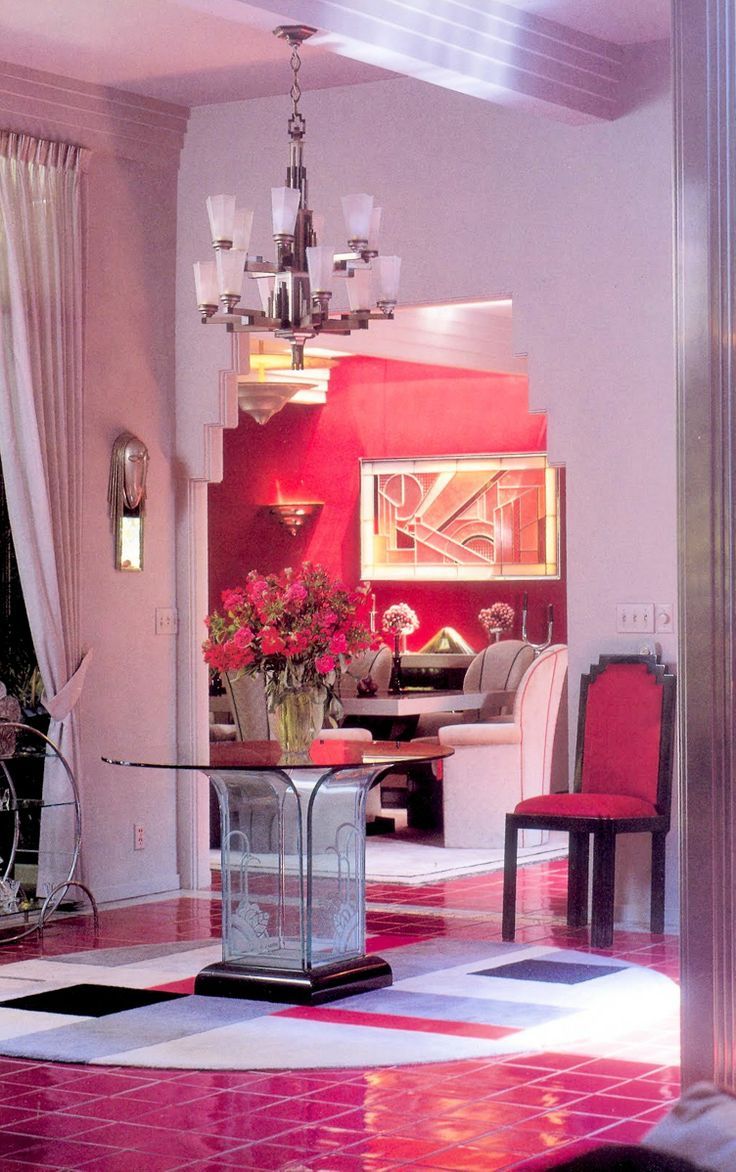 a dining room with red walls and pink flooring in the center is an elegant chandelier