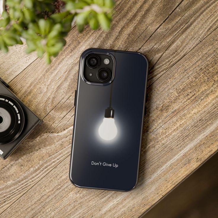 an iphone with a light bulb on it next to a camera and a plant in the background