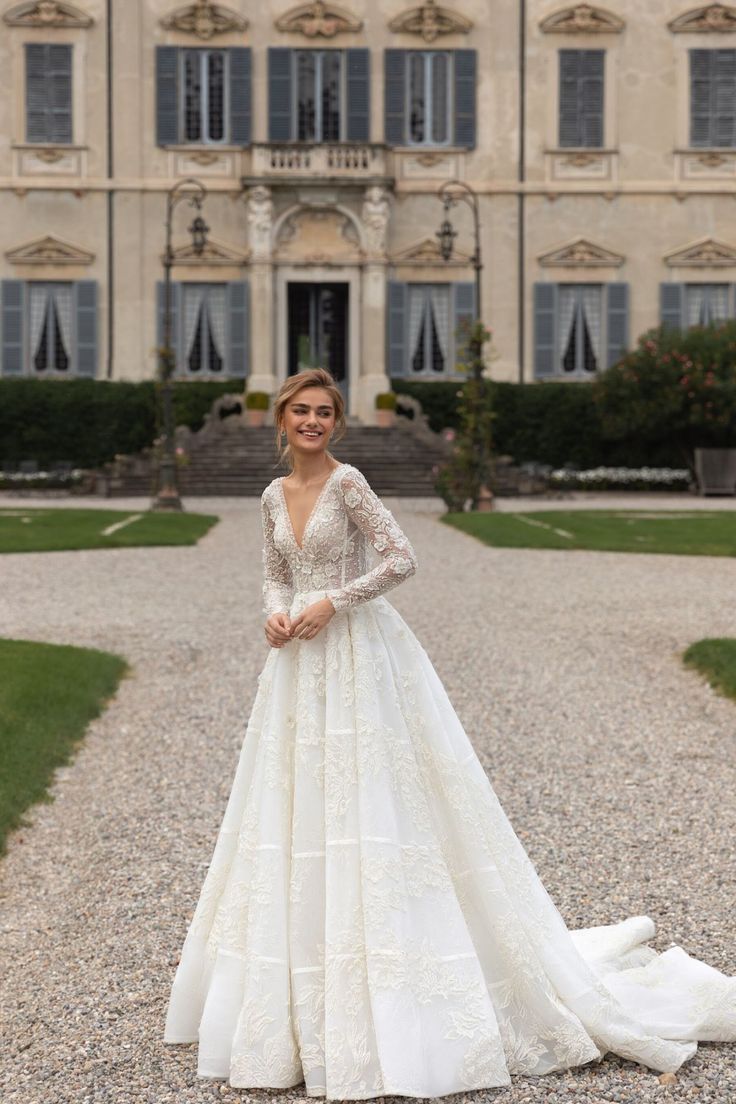 a woman standing in front of a large building wearing a long sleeved wedding dress