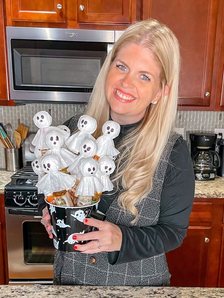 a woman holding a bucket full of halloween treats with ghost heads on them in the kitchen