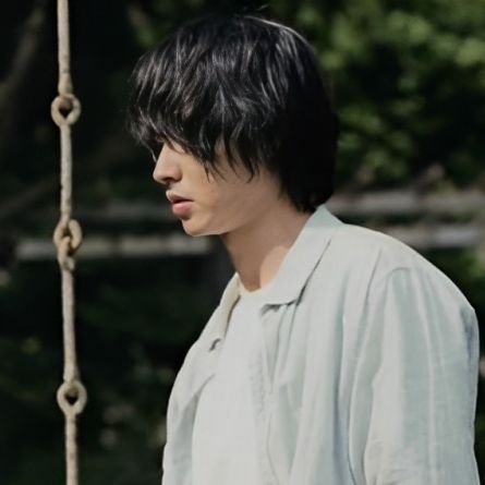 a man with black hair standing in front of a rope swing and looking off into the distance