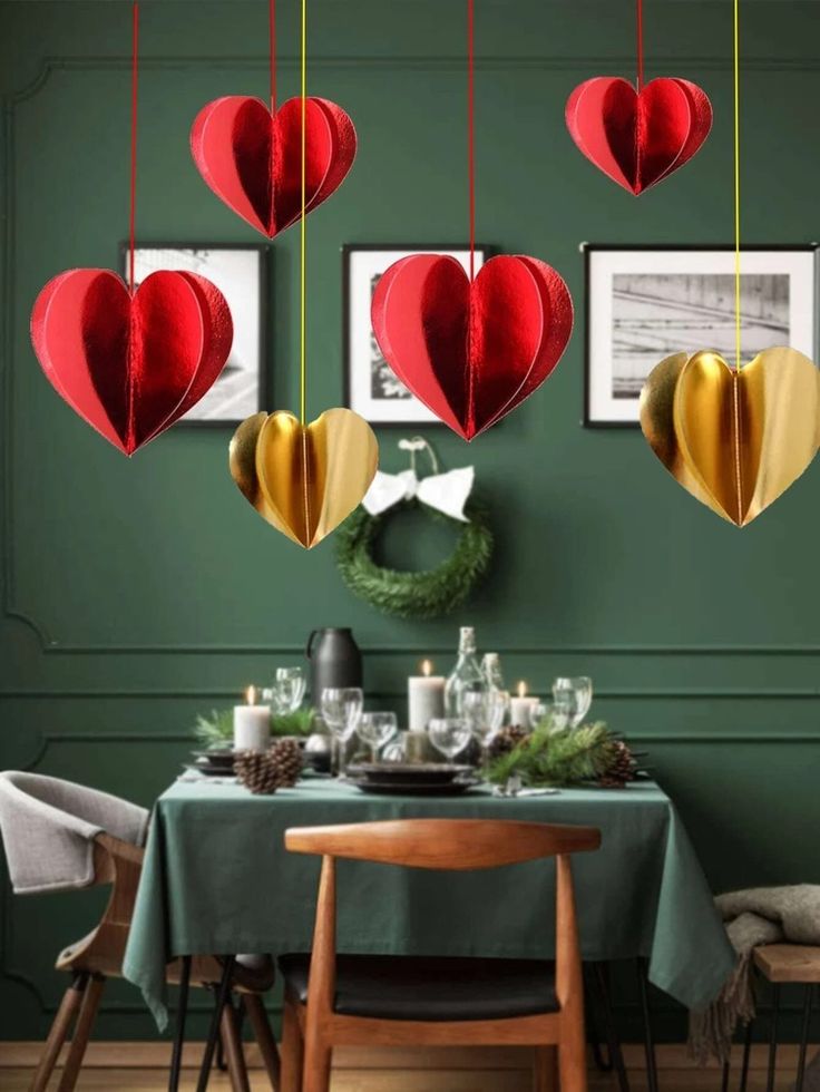 some red and gold paper hearts hanging from the ceiling above a dining room table with green walls