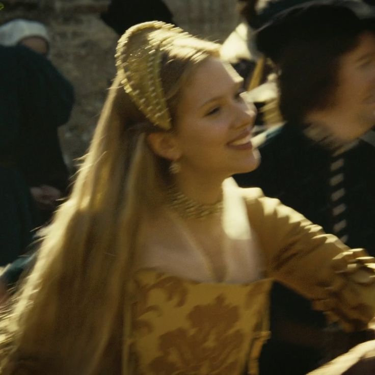 a woman with long blonde hair wearing a yellow dress and headdress in front of other people