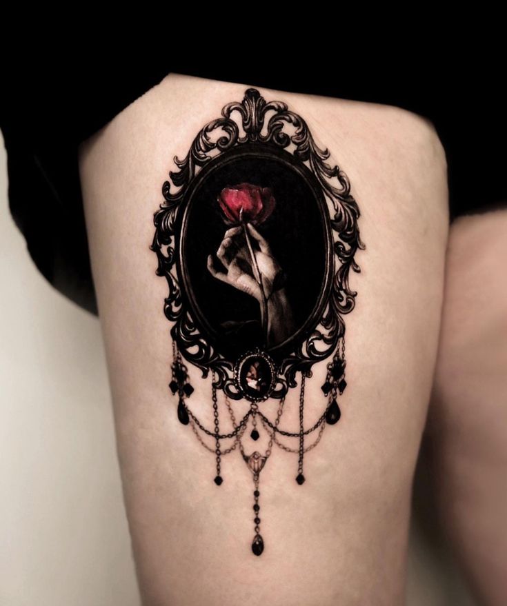 a woman's thigh with a black and red tattoo on it, holding a rose