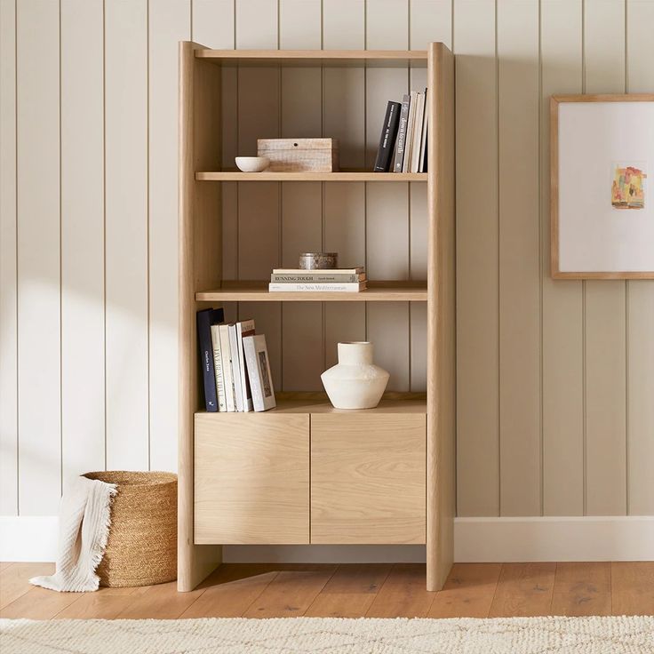 a wooden shelf with books and vases on it next to a white rug in a room