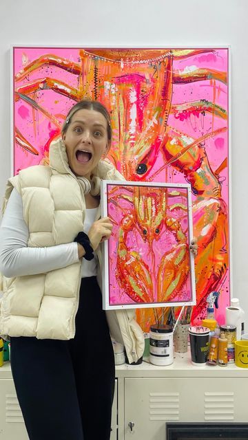 a woman standing in front of a painting holding up a piece of art with her mouth open